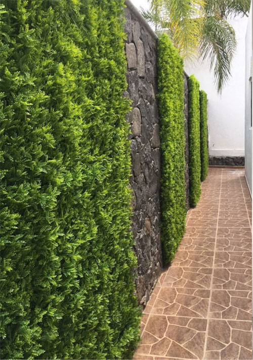Muro decorado con seto artificial y piso exterior, ideal para complementar espacios con persianas y pisos modernos.