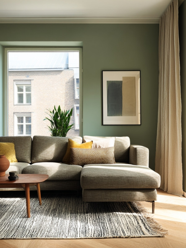 Sala decorada con paredes verde salvia, piso laminado roble claro y cortinas de lino.